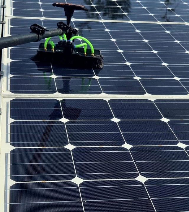 Cleaning a solar panel array with a brush attachment on a pole